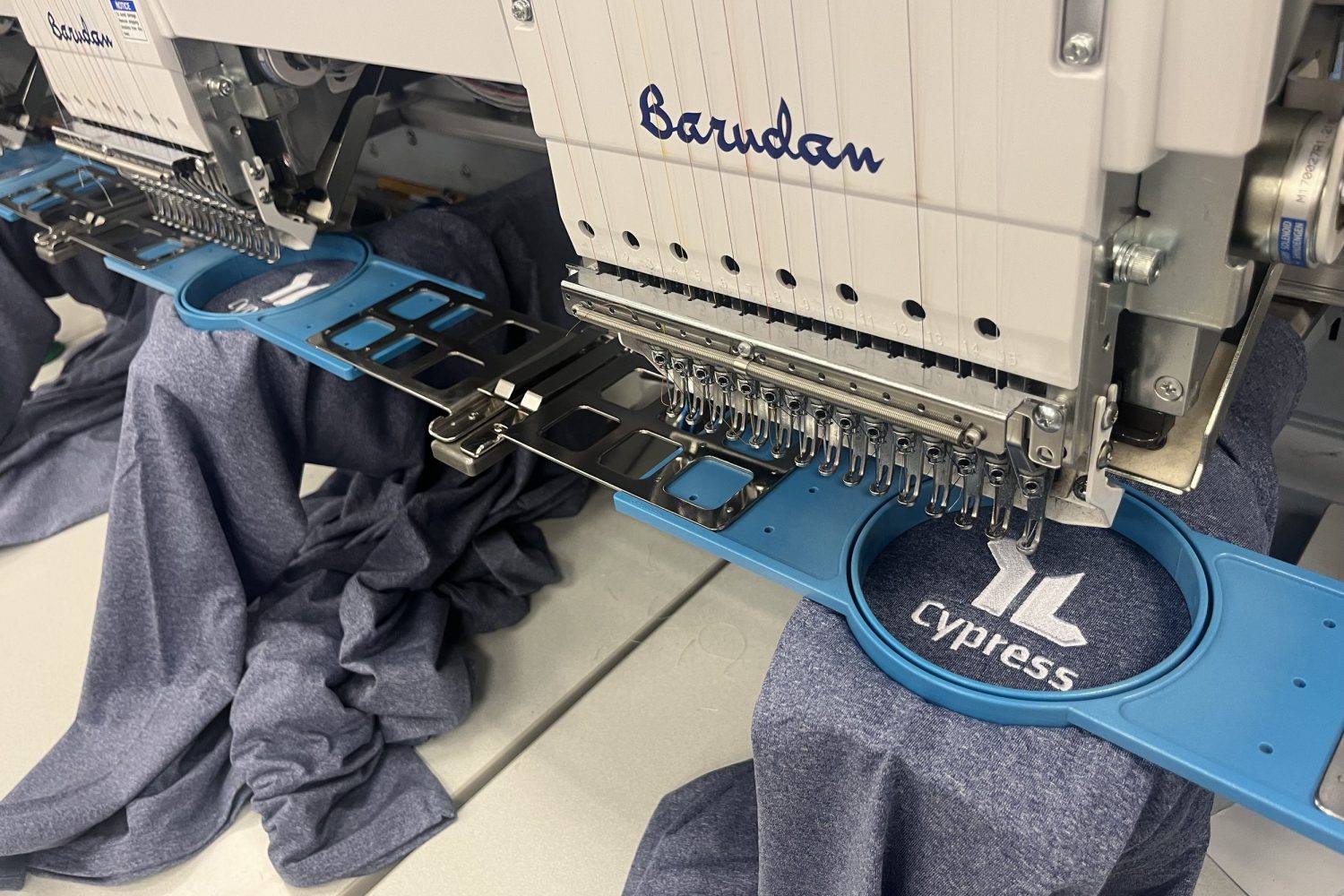 Barudan embroidery machine stitching Cypress Young Life logos on Nike Dri-fit shirts at Bayou Banners & Prints